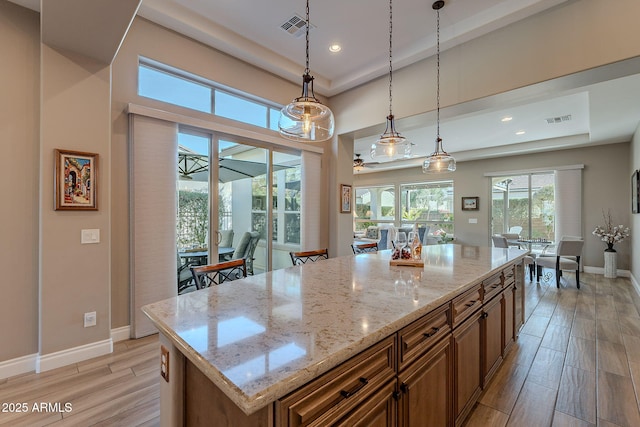 kitchen featuring hanging light fixtures, a raised ceiling, light stone countertops, and a center island