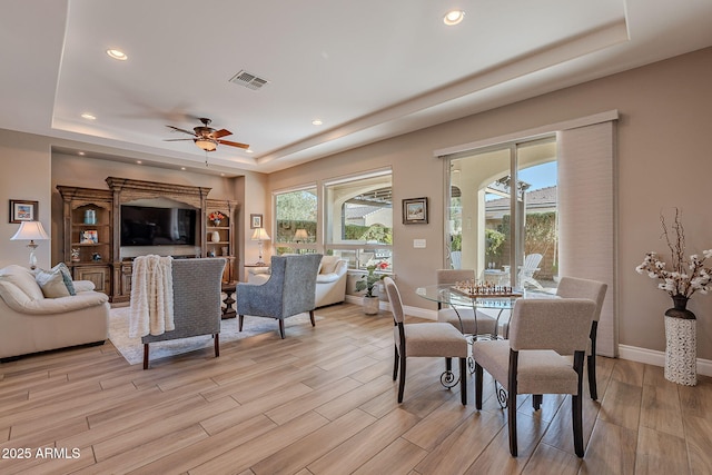 dining space featuring ceiling fan, a tray ceiling, a wealth of natural light, and light wood-type flooring