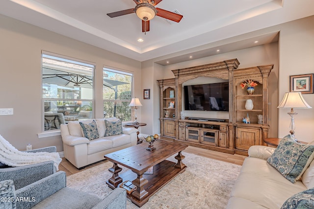 living room with a tray ceiling, ceiling fan, and light hardwood / wood-style flooring