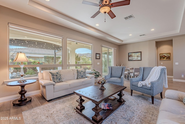 living room with ceiling fan, a raised ceiling, and light hardwood / wood-style flooring