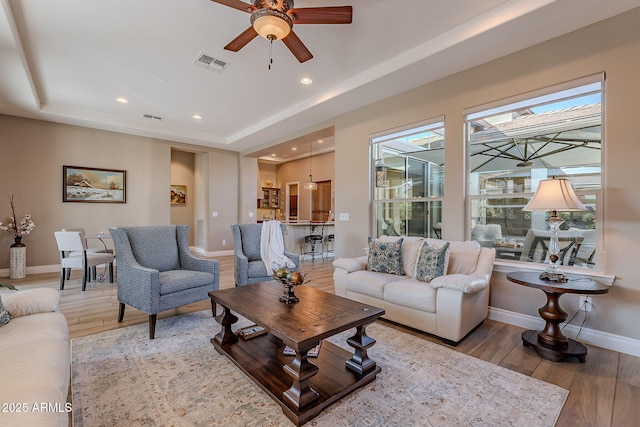 living room featuring ceiling fan, a tray ceiling, and hardwood / wood-style floors