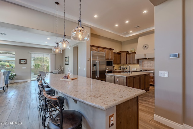 kitchen with hanging light fixtures, a kitchen breakfast bar, built in appliances, an island with sink, and decorative backsplash