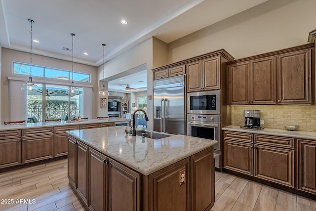 kitchen featuring sink, built in appliances, decorative light fixtures, a center island with sink, and light stone countertops