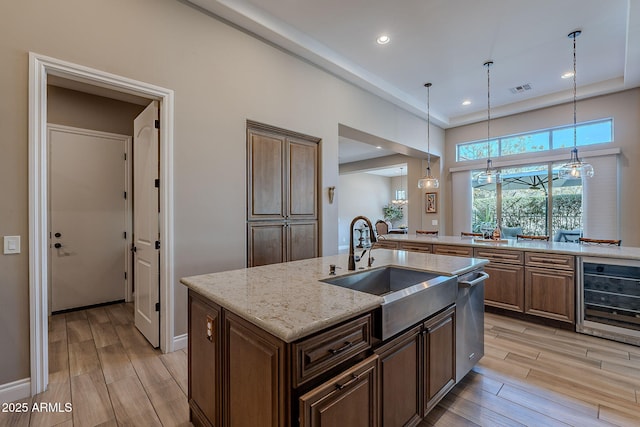 kitchen with sink, light stone counters, pendant lighting, beverage cooler, and a kitchen island with sink