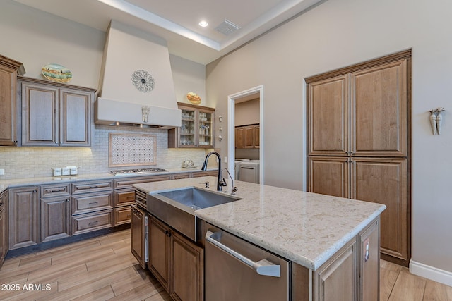 kitchen featuring stainless steel appliances, an island with sink, custom range hood, and tasteful backsplash