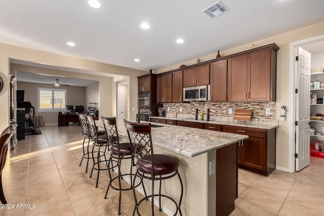 kitchen with a kitchen breakfast bar, light stone counters, stainless steel appliances, a kitchen island with sink, and light tile patterned floors