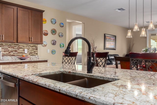 kitchen featuring decorative backsplash, light stone counters, sink, dishwasher, and hanging light fixtures