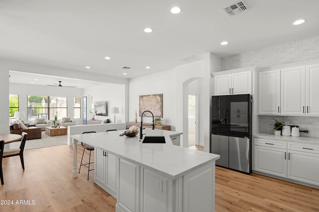 kitchen featuring stainless steel fridge, a center island with sink, sink, white cabinets, and light hardwood / wood-style flooring