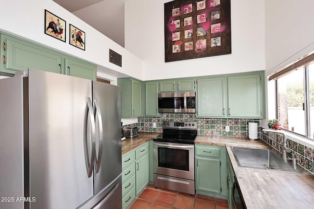 kitchen with tasteful backsplash, appliances with stainless steel finishes, green cabinets, and a towering ceiling