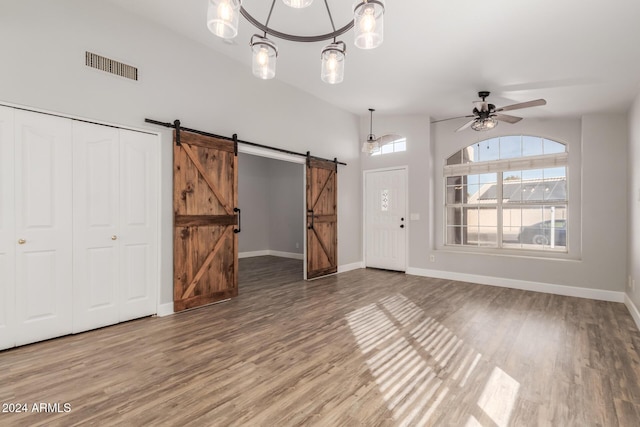 interior space featuring ceiling fan with notable chandelier, wood-type flooring, and a barn door