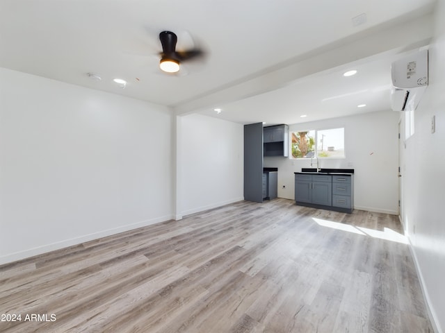 unfurnished living room with sink, light hardwood / wood-style floors, an AC wall unit, and ceiling fan