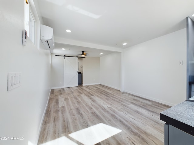 unfurnished living room with a barn door, a wall mounted air conditioner, and light wood-type flooring