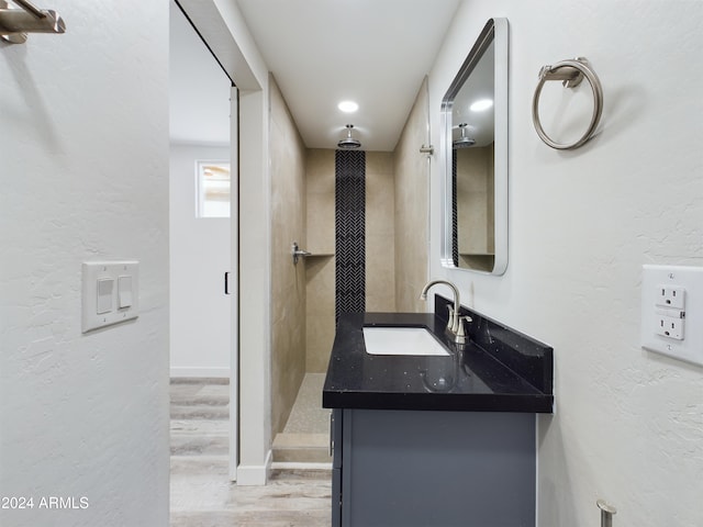 bathroom with hardwood / wood-style flooring, vanity, and tiled shower