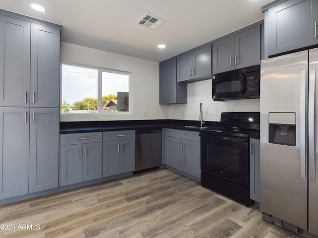 kitchen with gray cabinetry, light wood-type flooring, sink, and black appliances