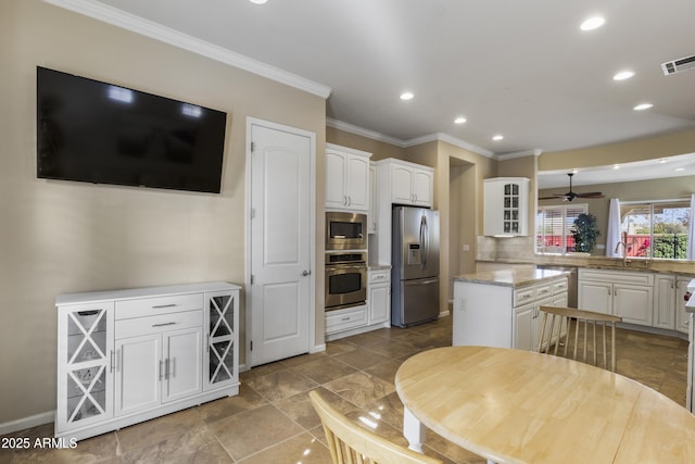 kitchen featuring white cabinetry, stainless steel appliances, a center island, light stone counters, and ornamental molding