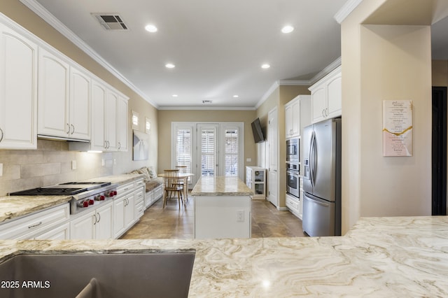 kitchen with crown molding, appliances with stainless steel finishes, light stone counters, white cabinets, and a kitchen island