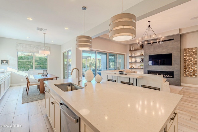 kitchen with dishwasher, sink, a kitchen island with sink, pendant lighting, and a fireplace