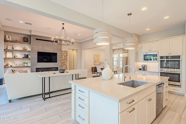 kitchen featuring stainless steel appliances, white cabinetry, decorative light fixtures, sink, and an island with sink