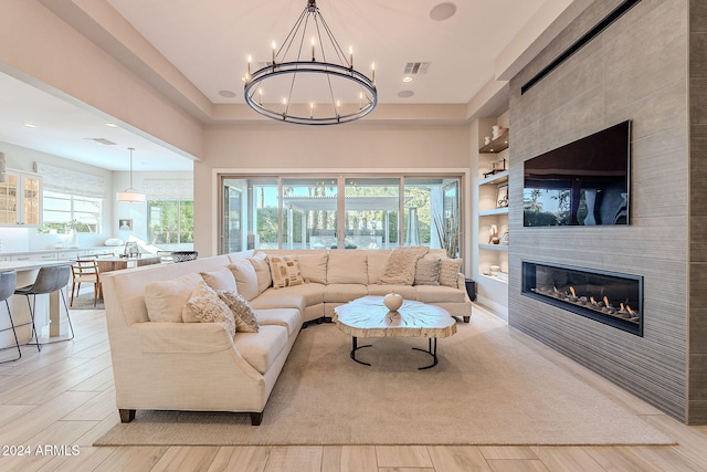 living room with a tiled fireplace, a wealth of natural light, light hardwood / wood-style flooring, and a chandelier