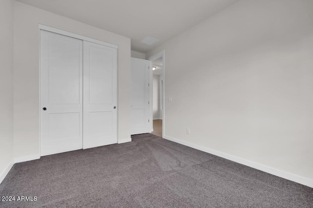 unfurnished bedroom with dark carpet, baseboards, and a closet
