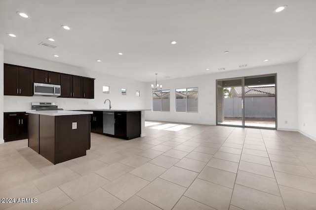kitchen with appliances with stainless steel finishes, a kitchen island, a chandelier, open floor plan, and light countertops