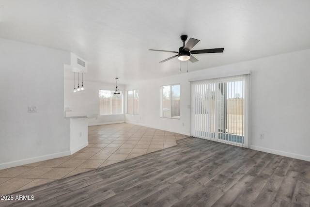 empty room with baseboards, visible vents, wood finished floors, and ceiling fan with notable chandelier
