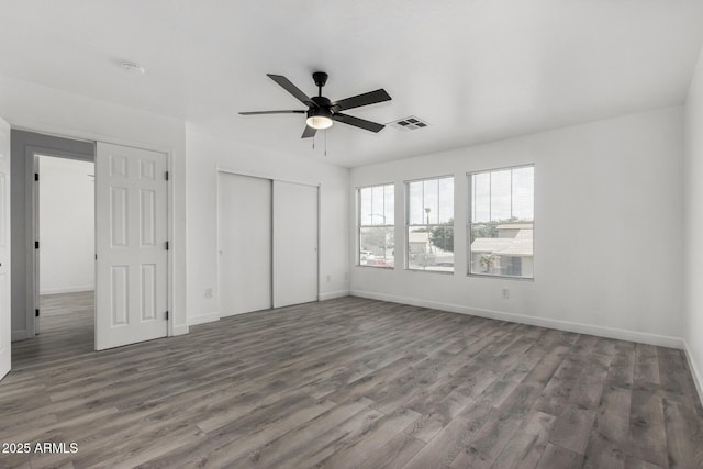 unfurnished bedroom featuring a closet, visible vents, baseboards, ceiling fan, and wood finished floors