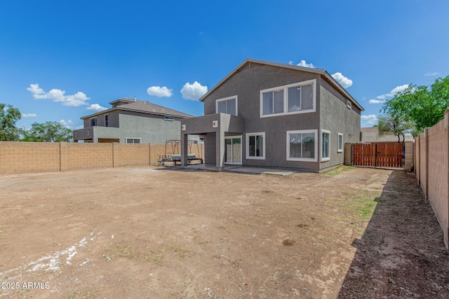 back of house with a fenced backyard, a gate, stucco siding, and a patio