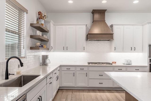 kitchen with custom range hood, white cabinetry, light hardwood / wood-style flooring, and sink