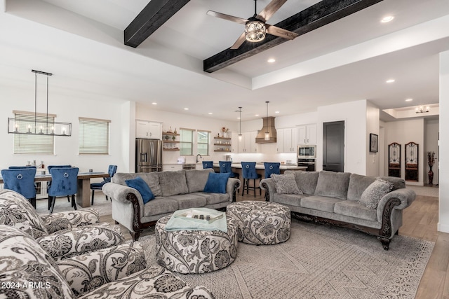 living room with ceiling fan with notable chandelier, beam ceiling, and light wood-type flooring