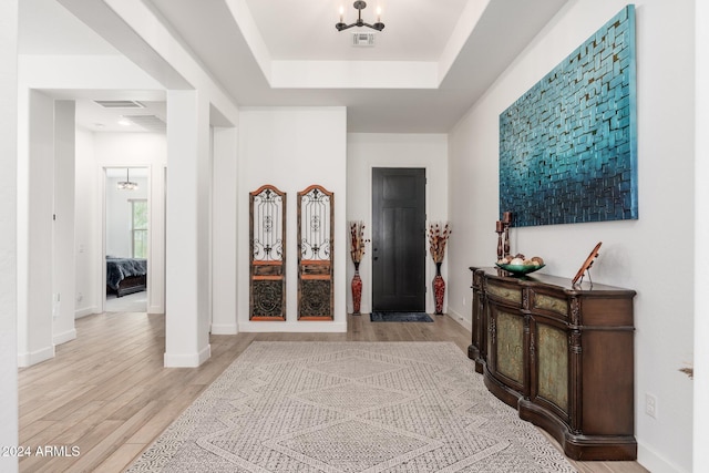 entryway with light hardwood / wood-style floors and a raised ceiling