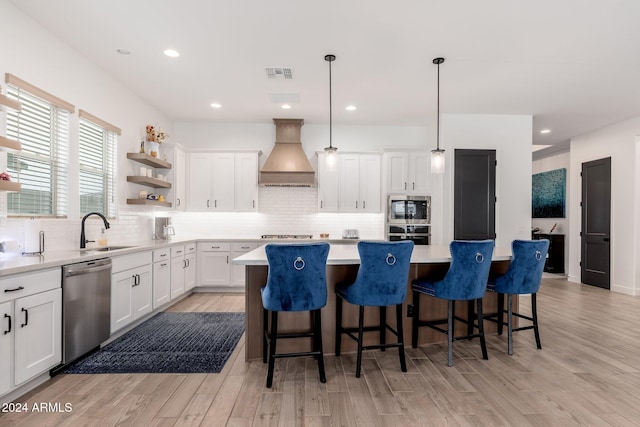 kitchen featuring white cabinetry, a center island, stainless steel appliances, premium range hood, and light hardwood / wood-style floors