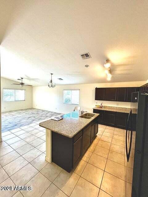 kitchen with light tile patterned flooring, light stone countertops, a wealth of natural light, and a center island with sink