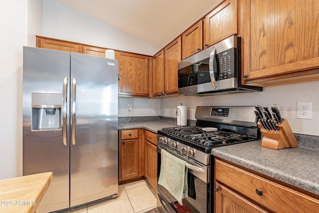 kitchen with vaulted ceiling, light tile patterned flooring, and appliances with stainless steel finishes