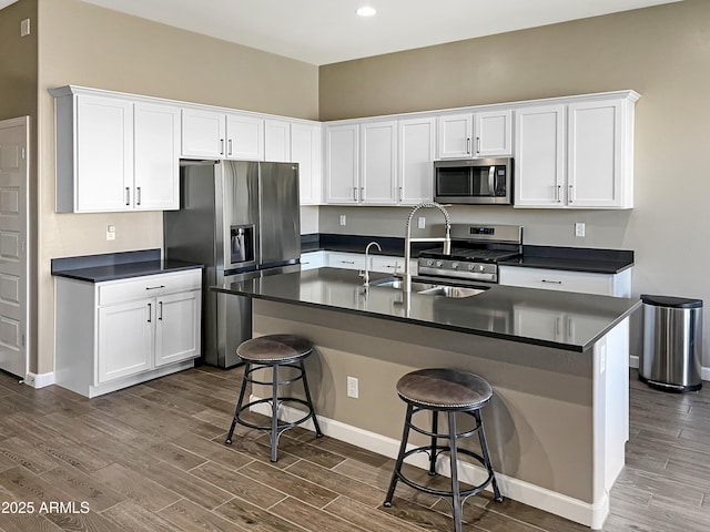 kitchen featuring dark wood-type flooring, dark countertops, appliances with stainless steel finishes, and a breakfast bar area