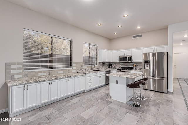 kitchen with appliances with stainless steel finishes, light stone countertops, a kitchen island, white cabinets, and decorative backsplash