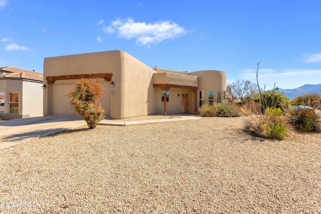 southwest-style home with a garage, driveway, a mountain view, and stucco siding