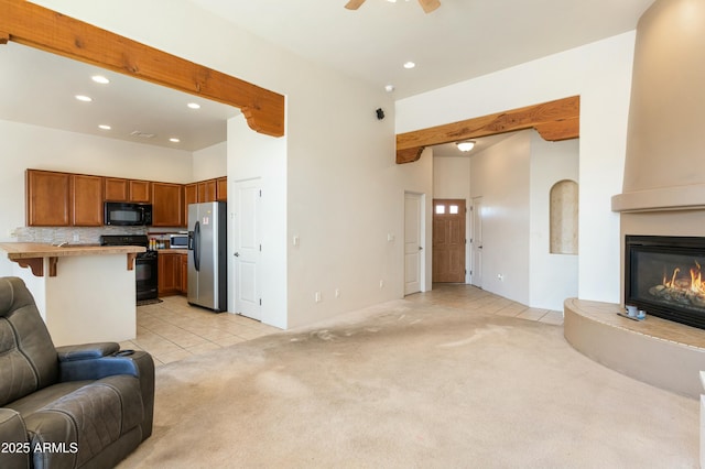 living area with recessed lighting, a glass covered fireplace, beam ceiling, and light colored carpet
