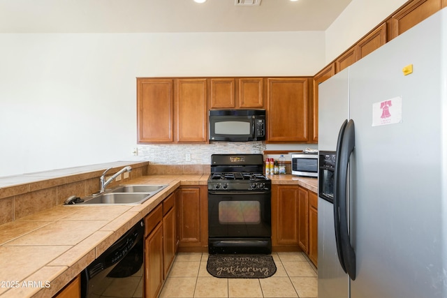 kitchen featuring tile countertops, light tile patterned floors, brown cabinetry, a sink, and black appliances
