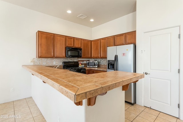 kitchen featuring a kitchen bar, brown cabinetry, a peninsula, and black appliances