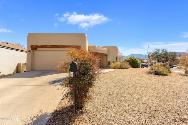 pueblo revival-style home with an attached garage, a mountain view, concrete driveway, and stucco siding
