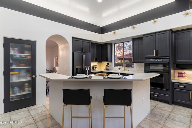 kitchen with light tile patterned floors, a kitchen breakfast bar, a kitchen island, decorative backsplash, and black appliances