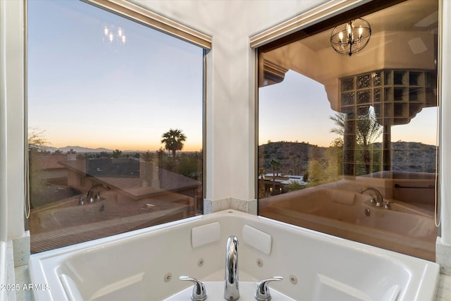 bathroom featuring a healthy amount of sunlight, a tub to relax in, and a chandelier