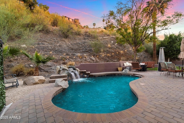 pool at dusk featuring a patio area, outdoor lounge area, and pool water feature