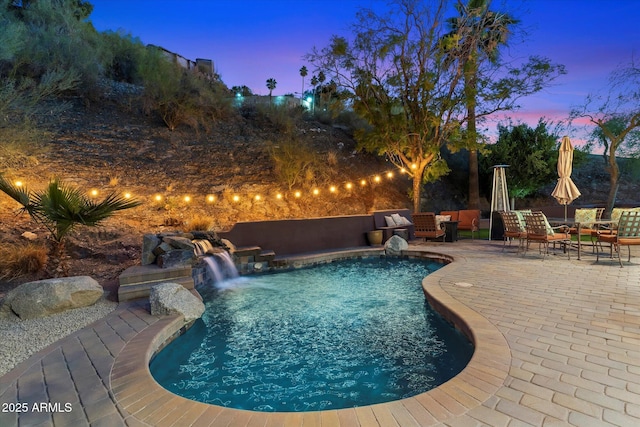 pool at dusk featuring a patio, an outdoor hangout area, and pool water feature