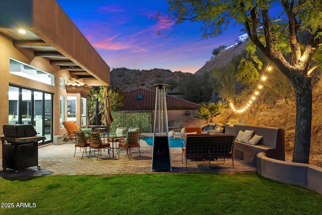 patio terrace at dusk featuring a grill, outdoor lounge area, a mountain view, and a lawn