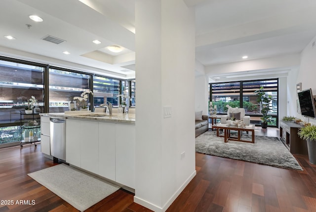 interior space with dark wood-style flooring, visible vents, white cabinets, a sink, and light stone countertops