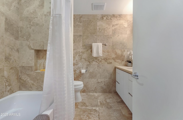 full bath featuring visible vents, toilet, shower / bath combo with shower curtain, vanity, and tile walls