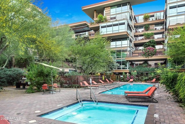 community pool with a patio area, a hot tub, and fence