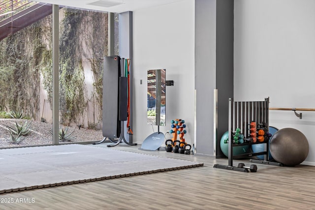 exercise room with floor to ceiling windows, visible vents, baseboards, and wood finished floors